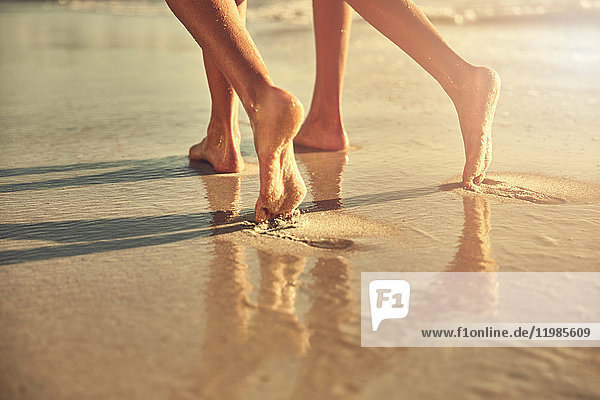 Nackte Füße von Frauen  die auf nassem Sand am sonnigen Sommerstrand laufen.