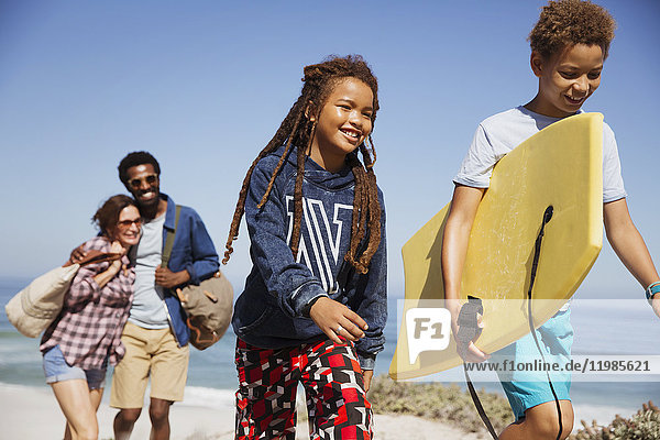 Lächelnde Familie mit Boogie-Board  Spaziergang auf sonnigem Sommerstrandweg
