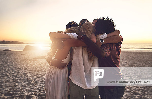Young friends hugging in a huddle on sunset summer beach