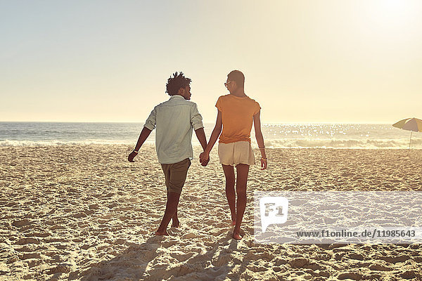 Young couple holding hands  walking on sunny summer beach