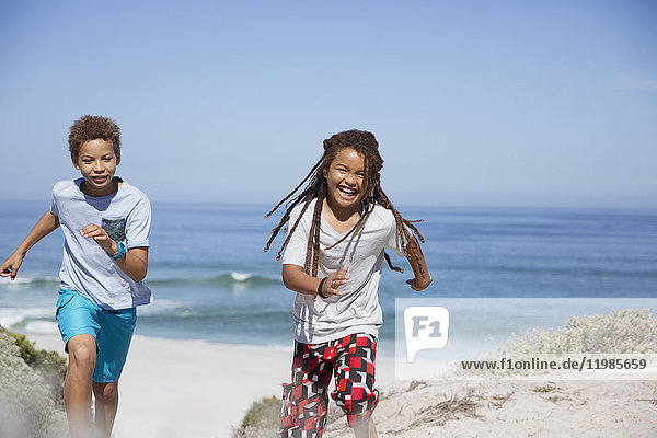 Verspielte Geschwister laufen am sonnigen Sommerstrand des Ozeans