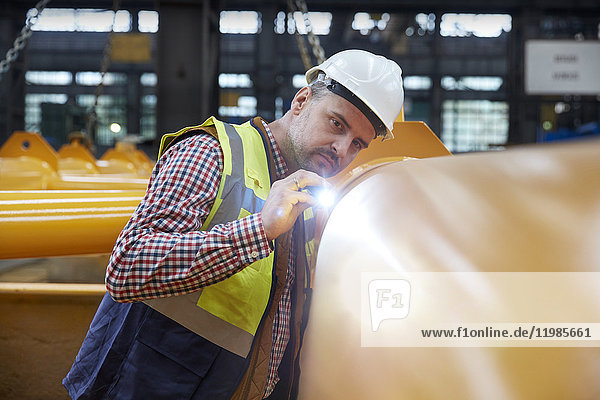 Fokussierter Ingenieur mit Taschenlampenprüfgerät in der Fabrik