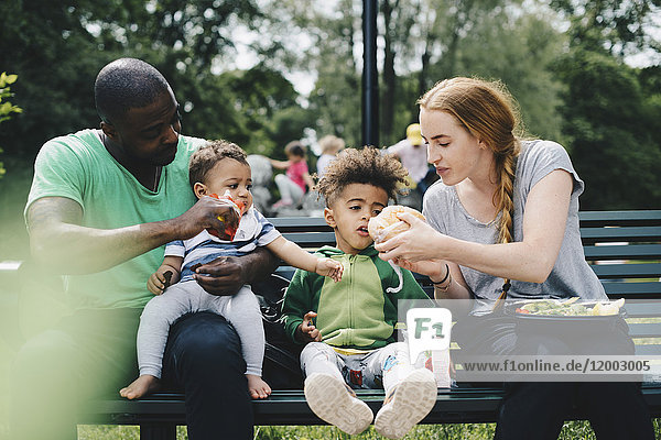 Parents feeding children while sitting on bench at park