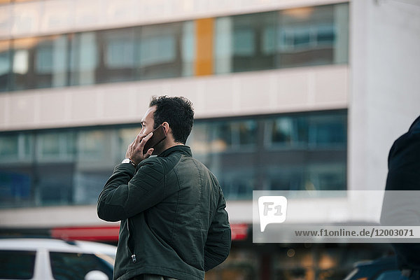 Mann spricht auf dem Handy  während er gegen das Gebäude in der Stadt steht.