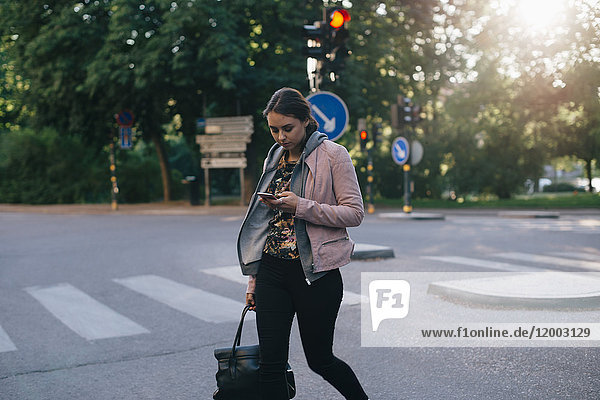 Junge Frau beim Überqueren der Straße mit dem Smartphone in der Stadt
