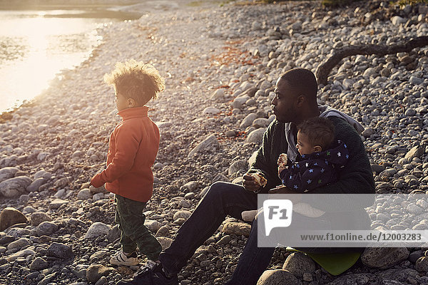 Vater sitzend mit Söhnen auf Felsen am Strand