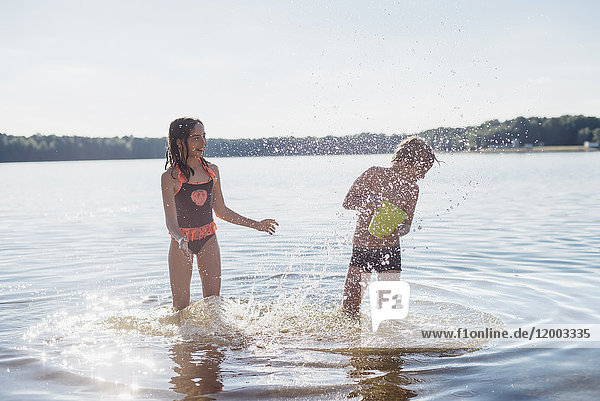 Junge und Mädchen spritzen mit Wasser am Seeufer