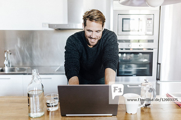 Porträt eines lächelnden Mannes in der Küche mit Laptop