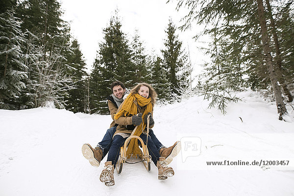 Happy young couple on sledge in winter forest