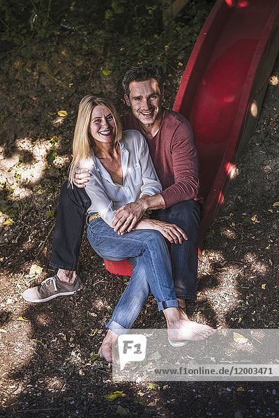 Happy couple sitting on slide in the woods
