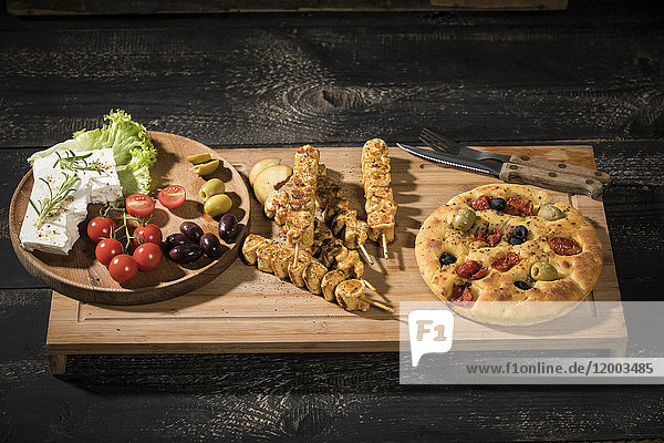 Fleischspieße  Fladenbrot  Schafskäse  Tomaten und Oliven auf Holzplatte