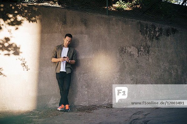 Mann steht an der Wand  während er ein Smartphone benutzt.