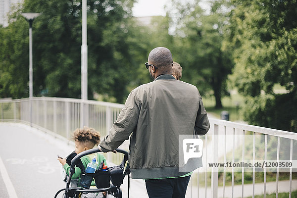 Rear view of father pushing baby stroller while walking with sons on bridge