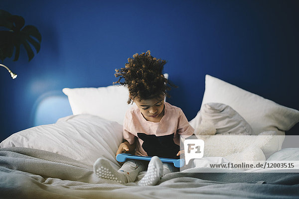 Junge mit digitalem Tablett  der zu Hause auf dem Bett sitzt