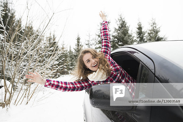 Porträt einer lachenden jungen Frau  die sich aus dem Autofenster lehnt.