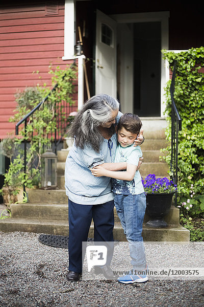 Großmutter umarmt Enkel im Hinterhof gegen Haus
