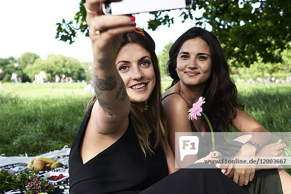 Friends taking smartphone selfies in the park