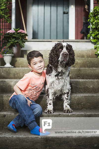Portrait of smiling boy sitting with English Springer Spaniel on steps in back yard