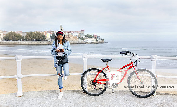 Spanien  Gijon  junge Frau mit Handy und Kopfhörer an der Uferpromenade