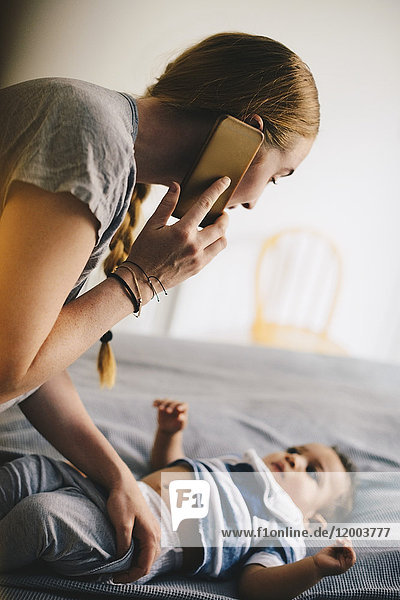 Mutter kleidet Kleinkind beim Telefonieren zu Hause an