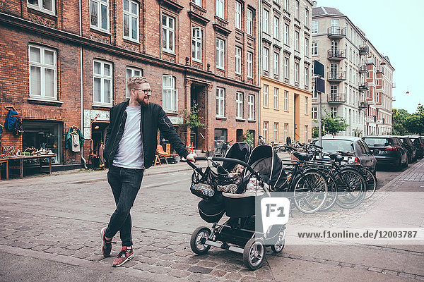 Full length of father standing by baby carriage on street in city