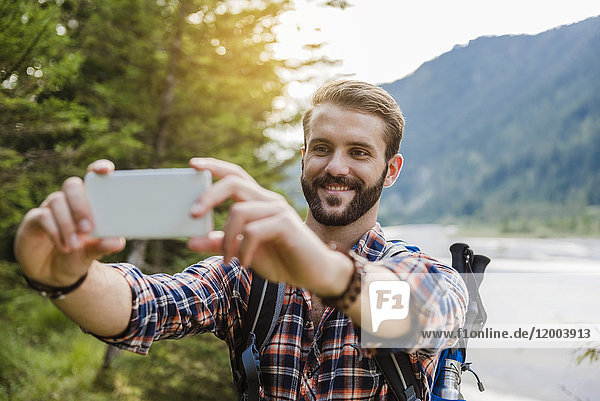 Porträt eines lächelnden jungen Wanderers  der sich mit dem Handy selbstständig macht.
