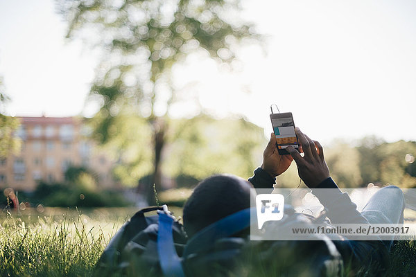Junger Mann  der ein Smartphone benutzt  während er auf Gras liegt.