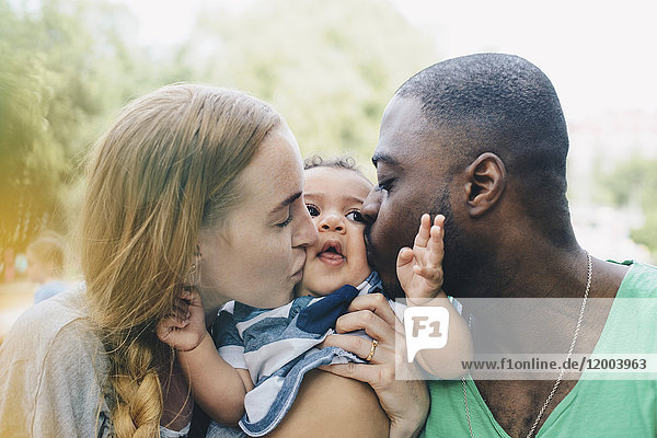 Nahaufnahme von multiethnischen Eltern  die ihren Sohn küssen.