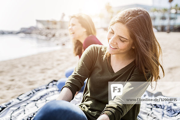 Zwei glückliche junge Frauen sitzen am Strand.