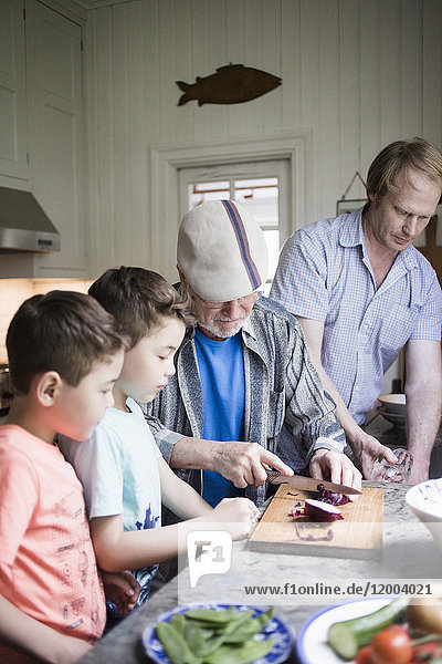 Enkel sehen Großvater beim Zwiebelschneiden an Bord  während der Vater in der Küche arbeitet.