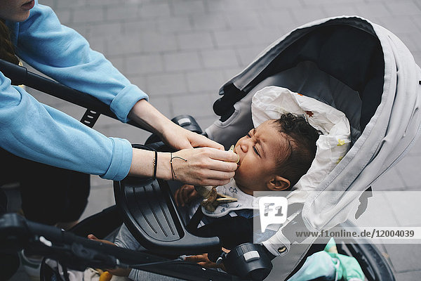 Abgeschnittenes Bild der Mutter  die den Schnuller auf dem Mund des Babys auf dem Bürgersteig hält.