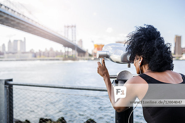 USA  New York City  Brooklyn  woman looking through coin-operated binoculars at Manhattan Bridge