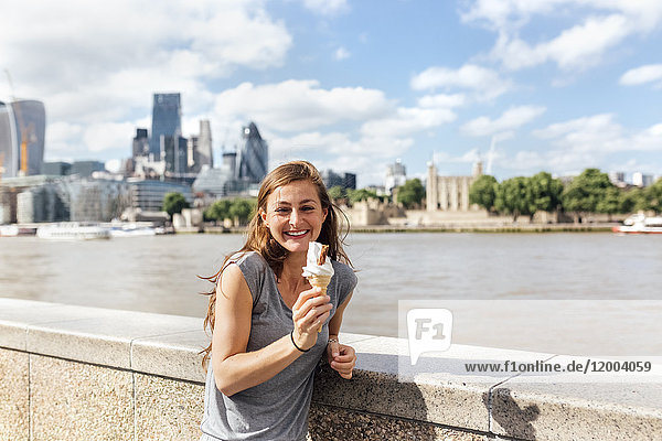 UK  London  glückliche Frau beim Essen eines Eises mit der Skyline im Hintergrund