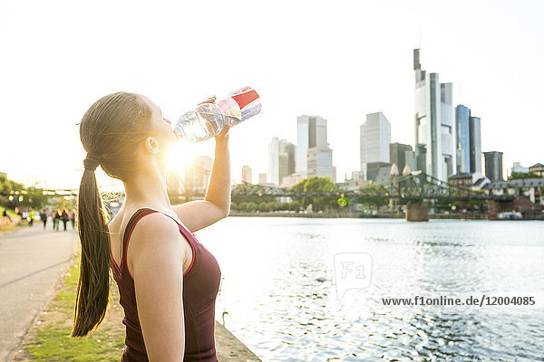 Deutschland  Frankfurt  sportliche junge Frau beim Trinken aus der Flasche am Flussufer