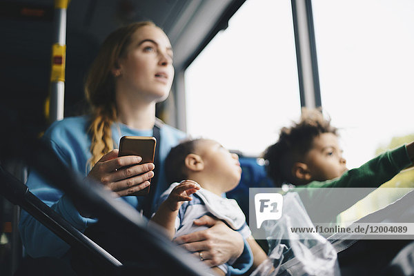 Mutter mit Kindern hält Handy beim Blick durchs Fenster aus dem Bus