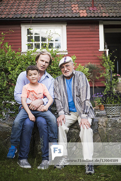 Portrait of man sitting with father and son against house in back yard