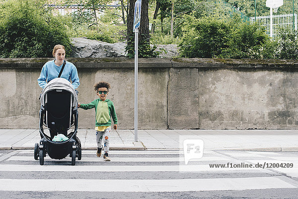 Mother pushing baby stroller while crossing road with son at city