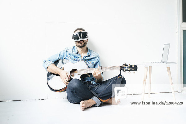 Mann mit Gitarre in Virtual Reality Brille auf dem Boden sitzend