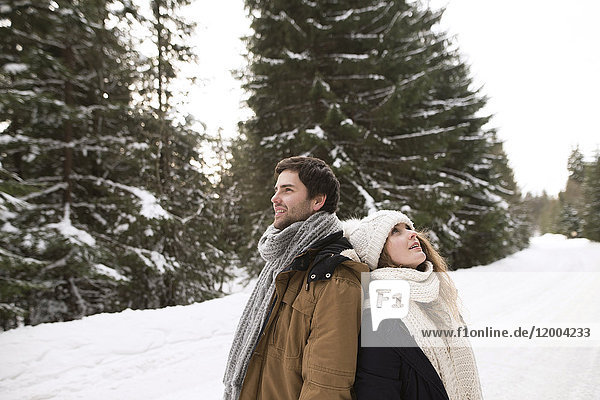 Happy young couple standing back to back in snow-covered winter landscape