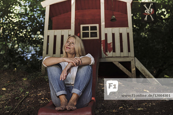 Mature woman sitting on slide in front of garden shed in the woods