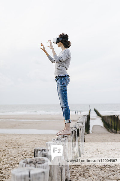 Frau auf Holzpfahl am Strand stehend mit VR-Brille