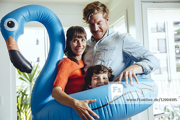 Happy parents with son holding an inflatable flamingo at home