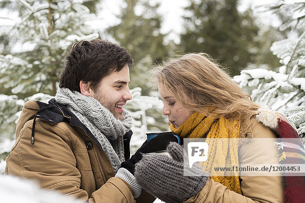 Young couple in love with cups of tea in winter forest