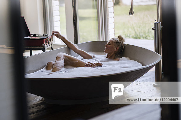 Mature woman taking bubble bath  listening music from analogue record player