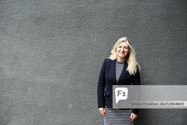 Porträt einer lächelnden Geschäftsfrau an der grauen Wand