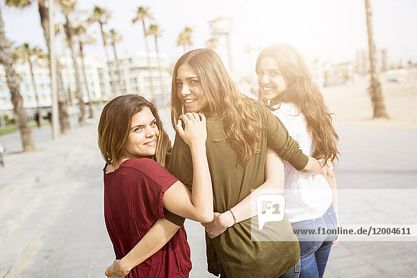 Drei glückliche Freundinnen beim Spaziergang auf der Strandpromenade