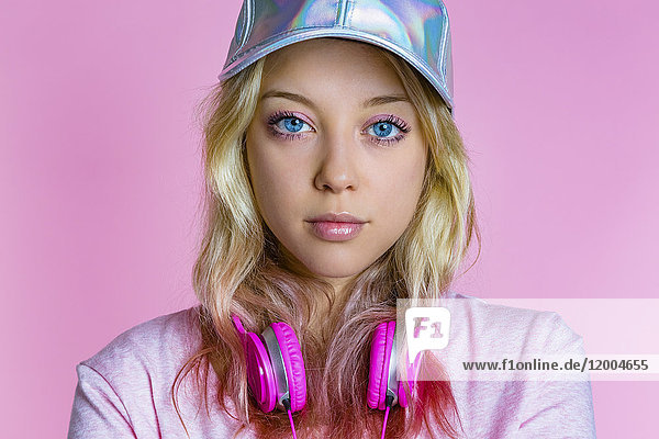 Portrait of young woman with headphones and basecap in front of pink background