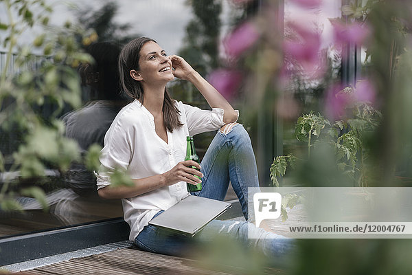 Happy woman with laptop and bottle sitting on balcony
