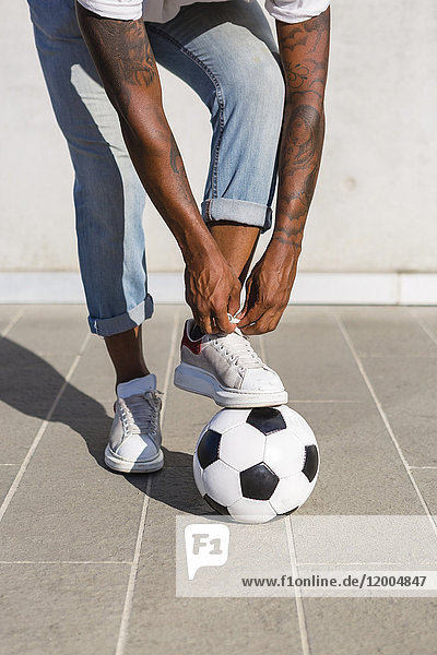 Young man tying his shoes on a soccer ball  partial view