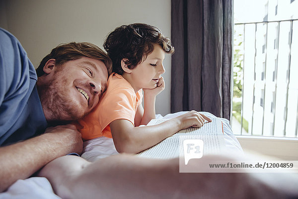Sohn liest seinem Vater im Bett vor.